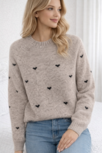 Woman wearing a beige sweater with black heart patterns against a white background