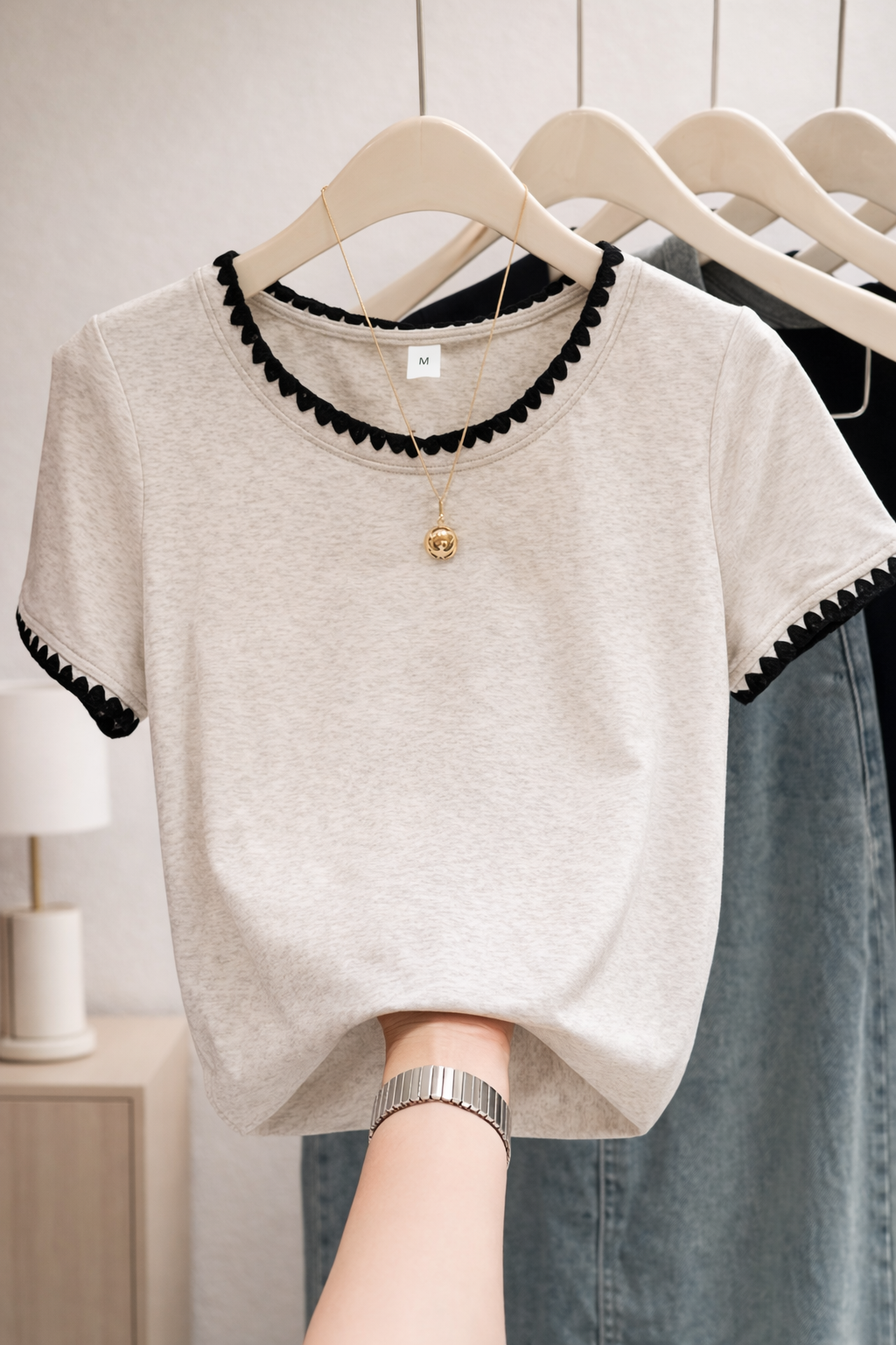 Beige t-shirt with black trim on a hanger against a neutral background