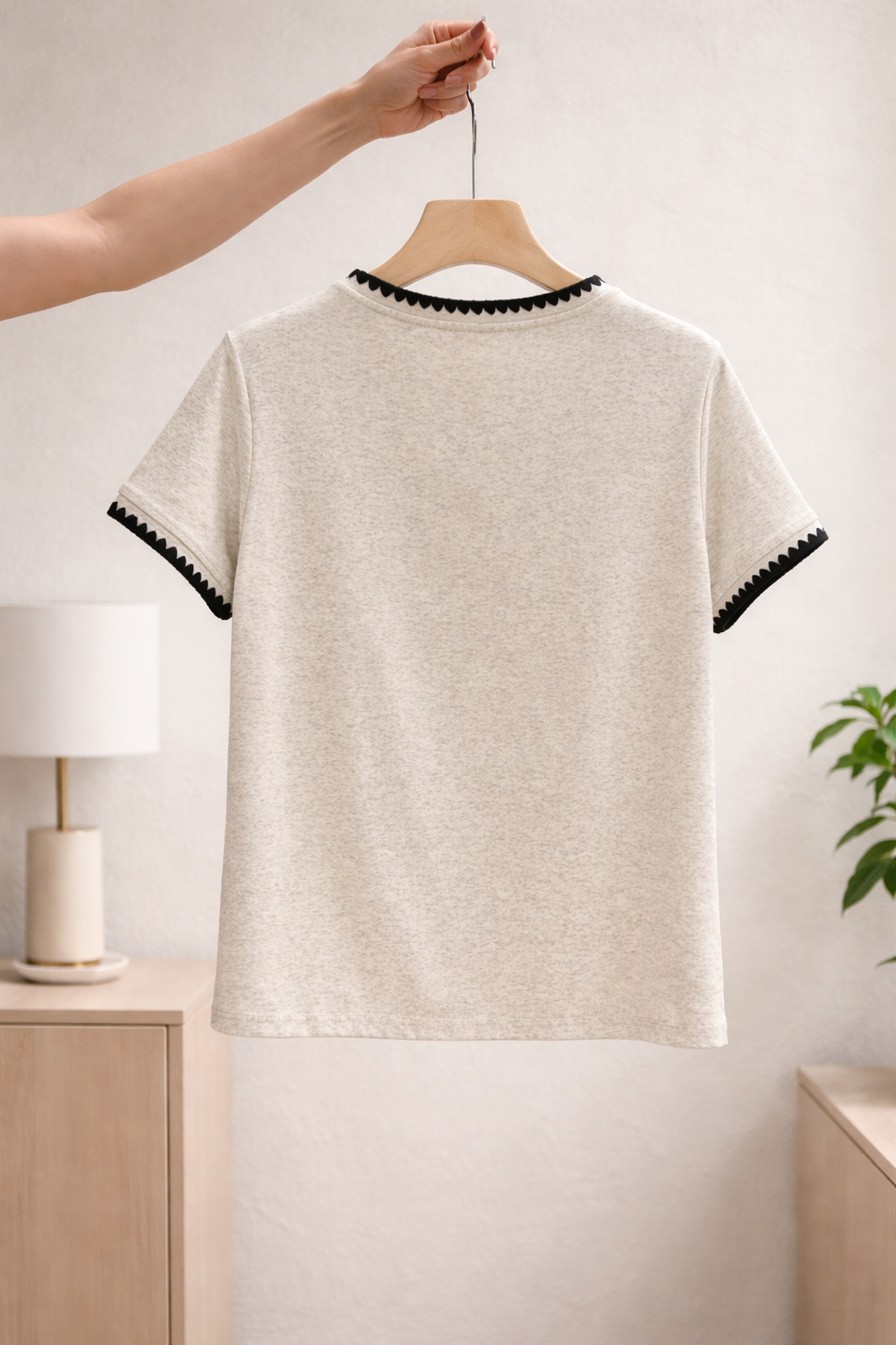 Beige t-shirt with black trim on a hanger against a neutral background