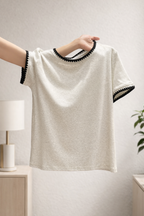 White t-shirt with black trim held by a person against a neutral background