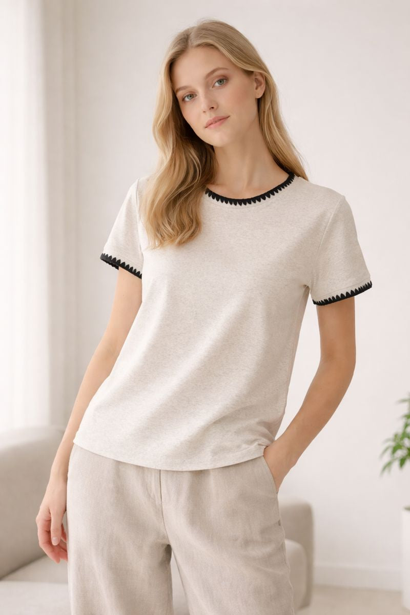 Woman wearing a white top with black trim in a minimalistic room.