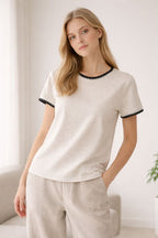 Woman wearing a white top with black trim in a minimalistic room.
