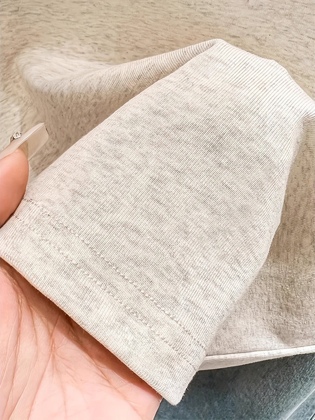 Close-up of beige fabric held by a hand on a neutral background