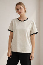 Woman wearing a beige t-shirt with black trim on a plain background