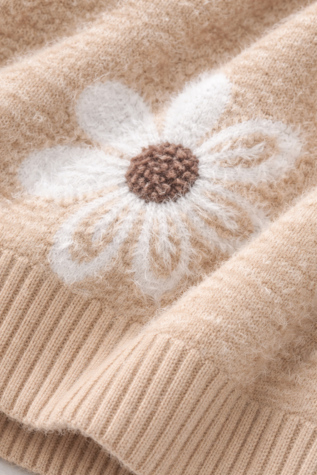 Close-up of a beige knitted fabric with a white flower design.