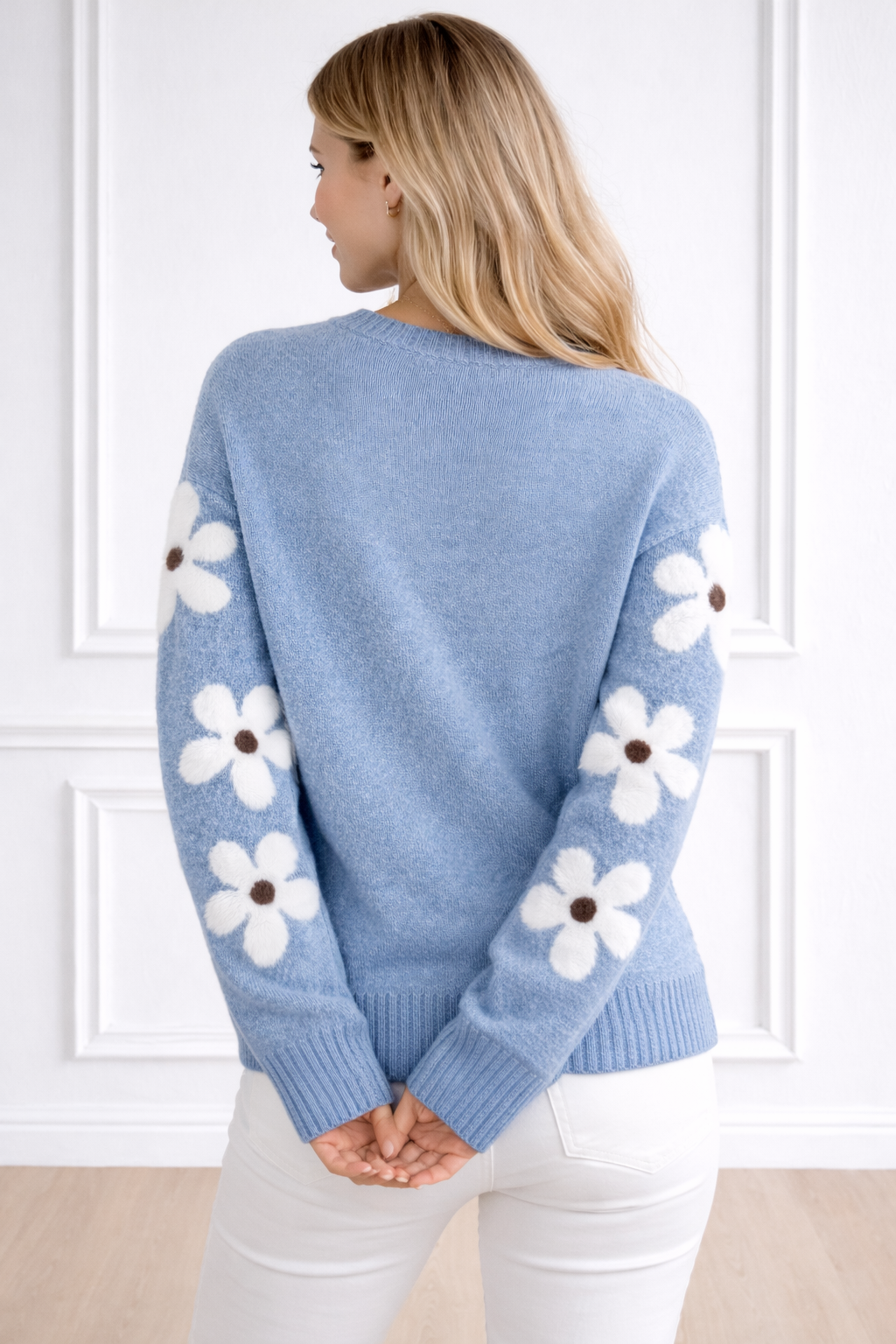 Light blue sweater with white floral patterns on sleeves against a white wall.