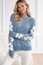 Woman wearing a blue sweater with white floral patterns indoors.