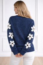 Woman wearing a blue sweater with white floral patterns in a minimal indoor setting