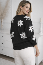Woman wearing a black sweater with white floral patterns in a room.