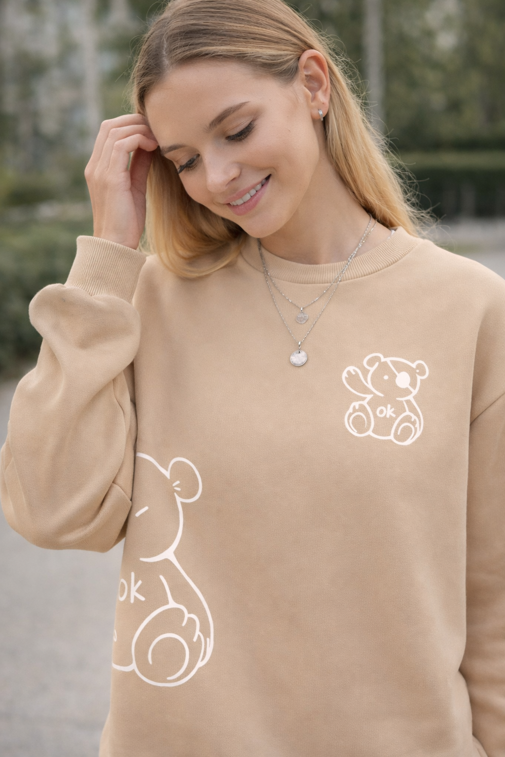 Woman wearing a beige sweatshirt with white graphics outdoors
