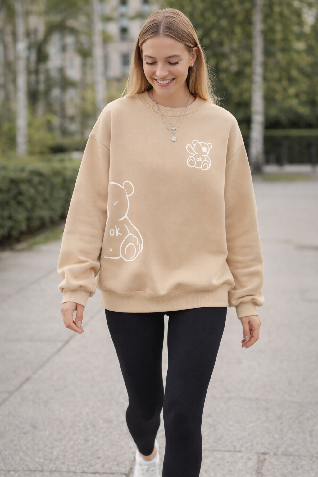 Woman wearing a beige sweatshirt with white graphics walking outdoors.