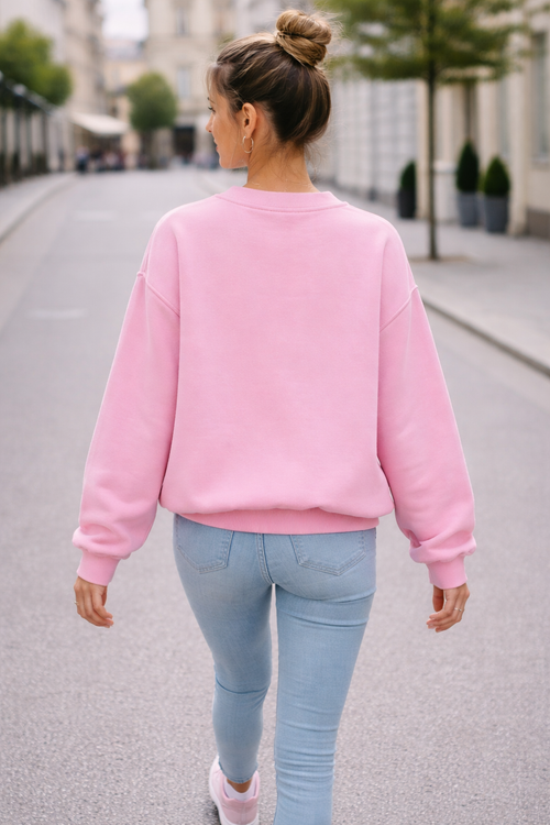 Person wearing a pink sweatshirt and light blue jeans walking on a street.