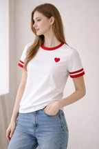 Woman wearing a white t-shirt with red accents and a heart design, paired with blue jeans.