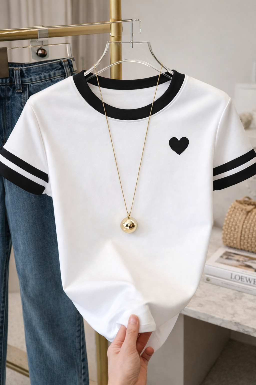 White shirt with black heart design and black trim on a hanger, held by a hand.
