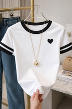 White shirt with black heart design and black trim on a hanger, held by a hand.