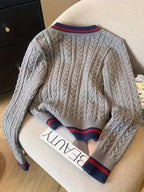 Gray cable knit sweater with blue and red accents on a chair