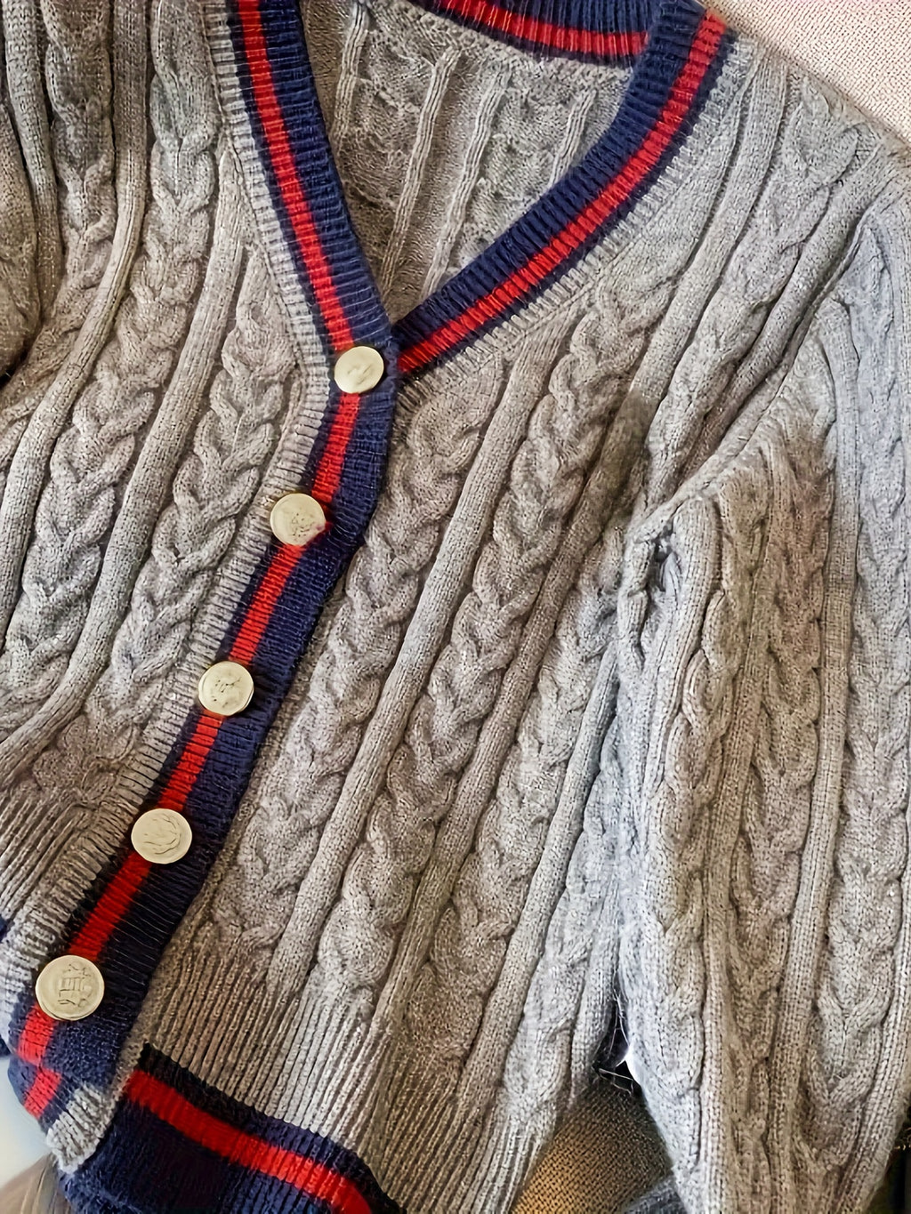 Close-up of a cable knit cardigan with red and blue trim and gold buttons.