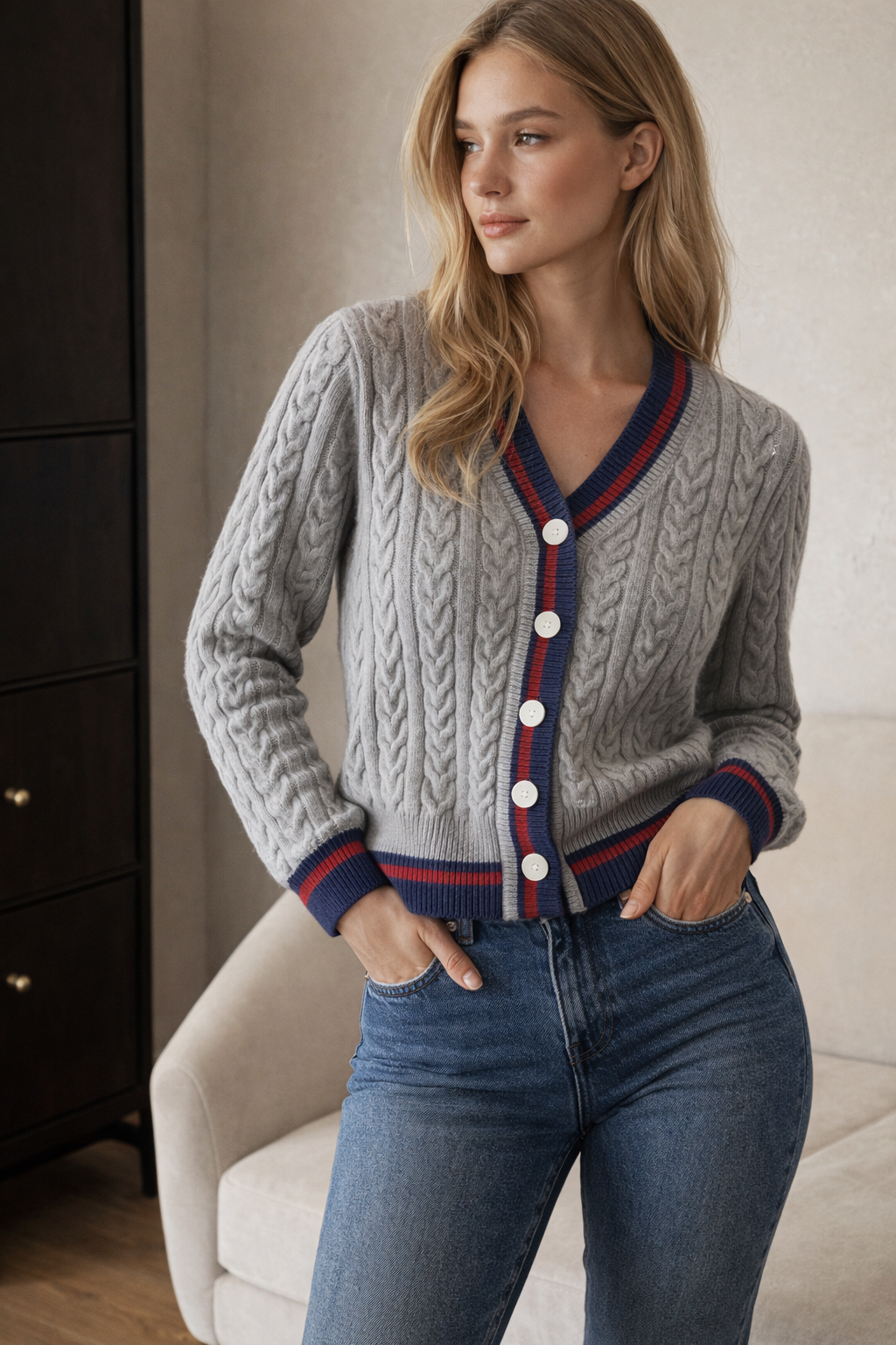 Woman wearing a gray cable knit cardigan with red and blue trim and blue jeans indoors.