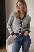 Woman wearing a gray cable knit cardigan with red and blue trim and blue jeans indoors.