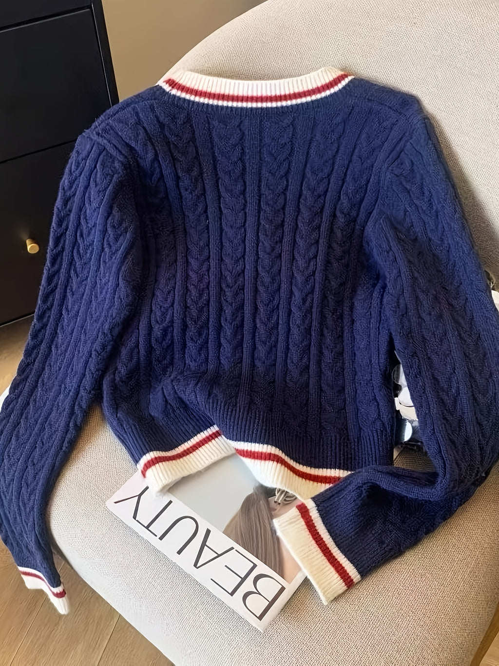 Blue cable knit sweater with red and white trim on a chair next to a magazine.