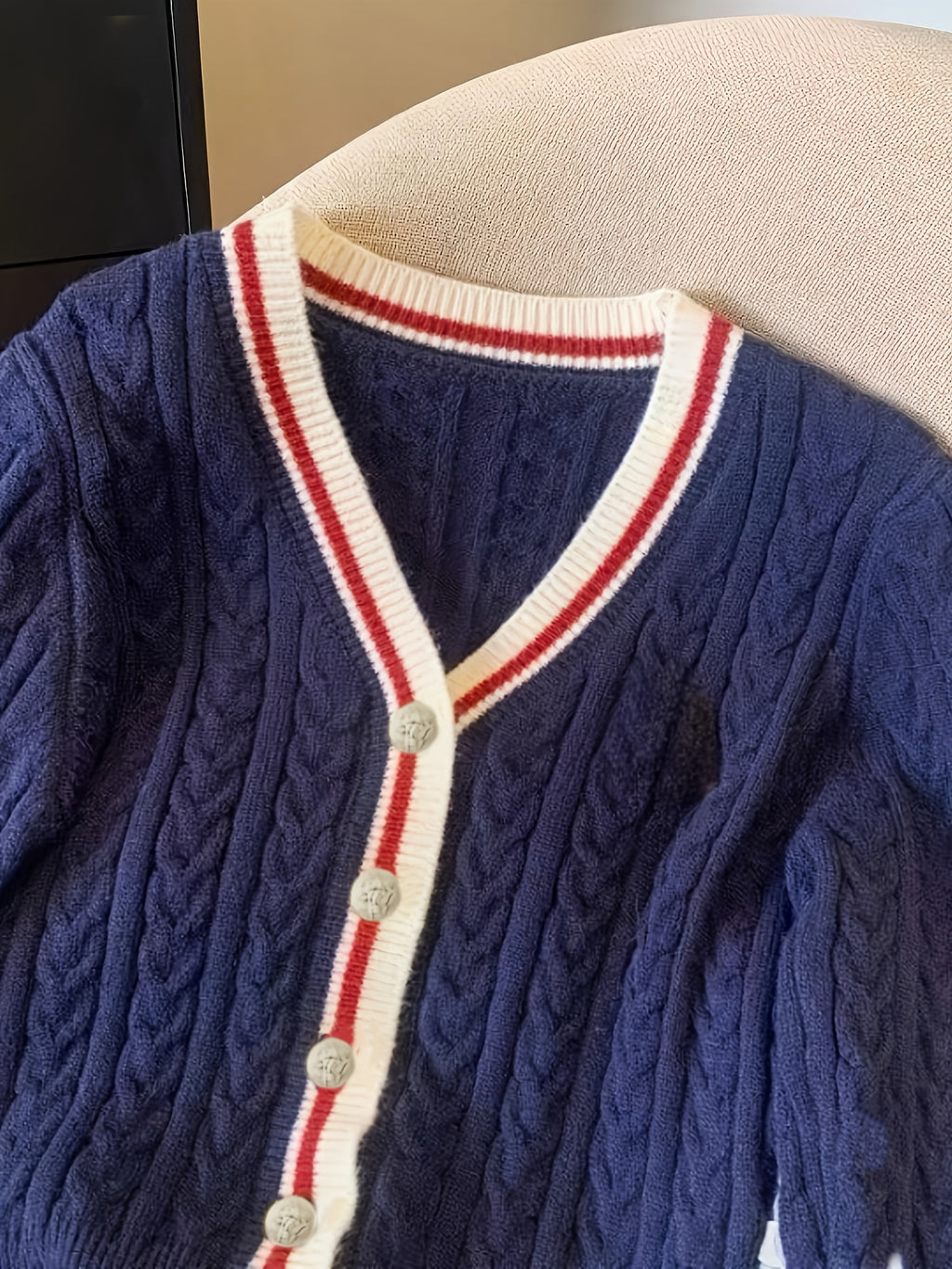 Blue cable knit cardigan with white and red trim on a mannequin
