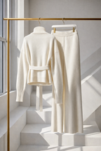 White outfit with a jacket and pants on a gold rack against a light gray wall.