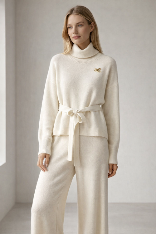 Woman wearing a cream-colored outfit with a logo on a plain background