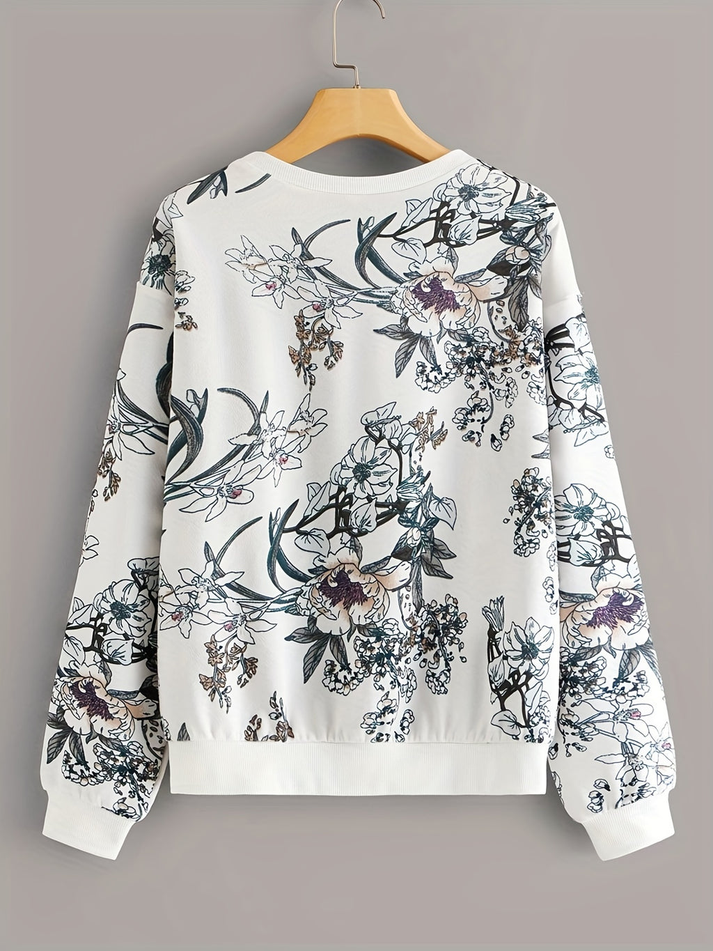 Floral patterned sweatshirt on a wooden hanger against a gray background