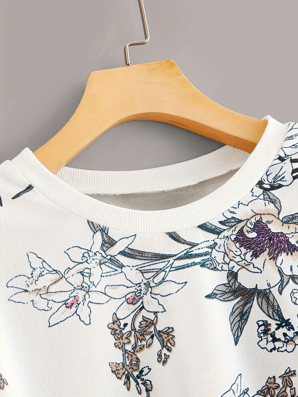 White shirt with floral embroidery on a wooden hanger against a gray background