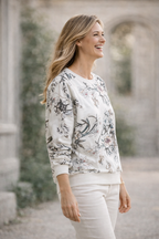 Woman wearing a floral sweatshirt and white pants standing outdoors.