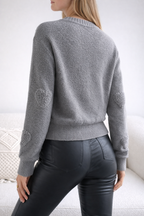 Person wearing a gray sweater with patch details on a white background