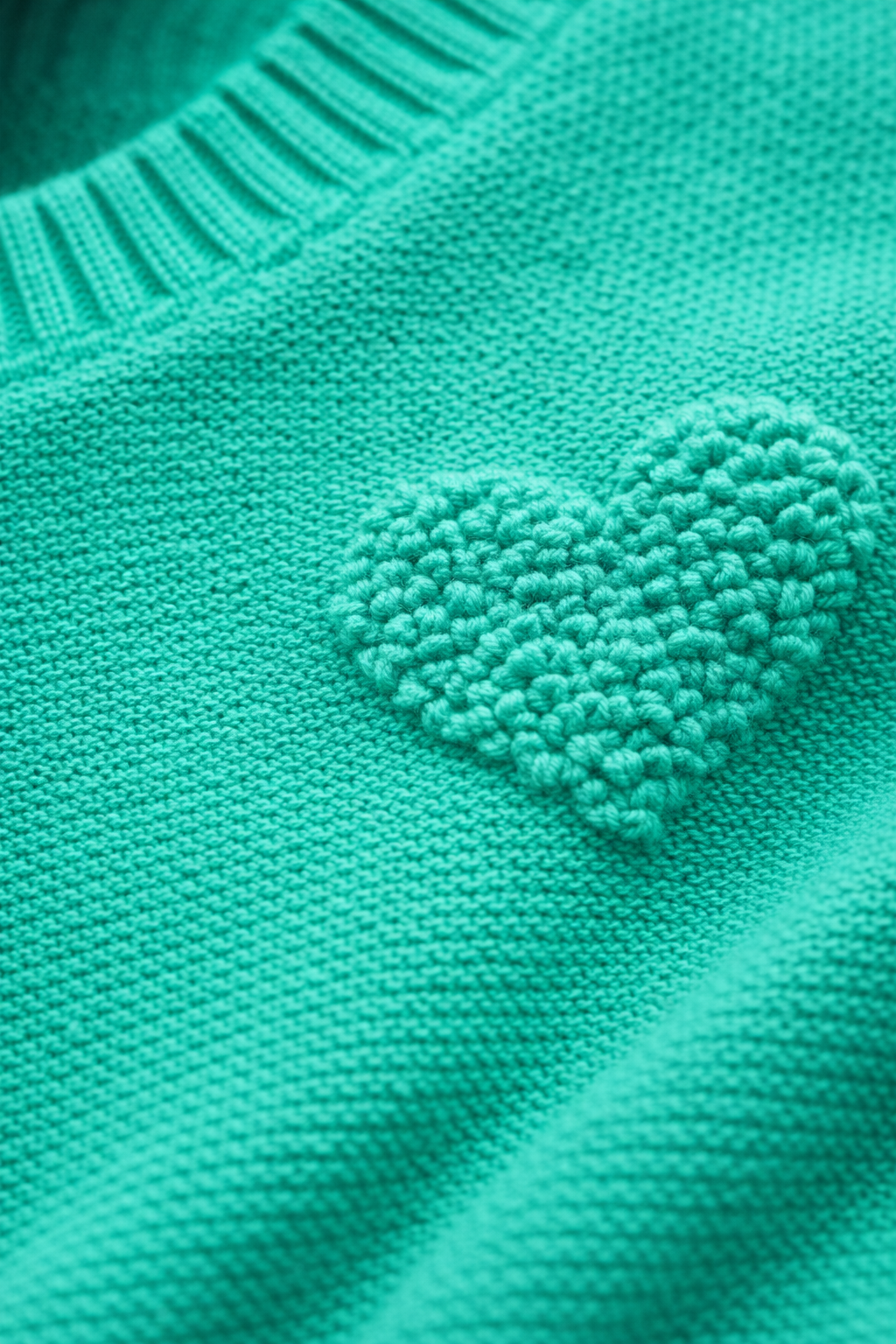 Close-up of a teal knitted sweater with a heart-shaped patch.