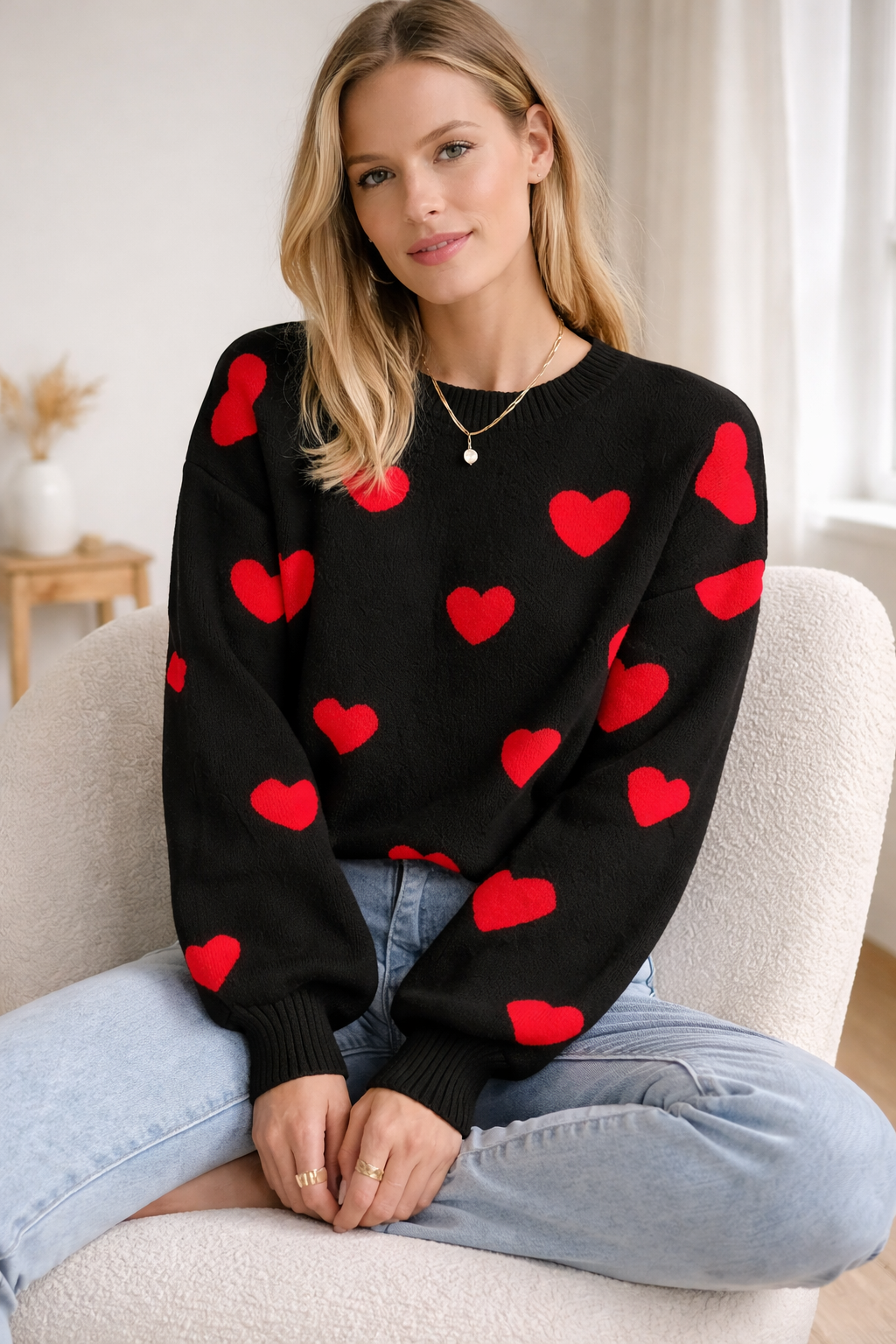 Woman wearing a black sweater with red heart patterns sitting on a couch.
