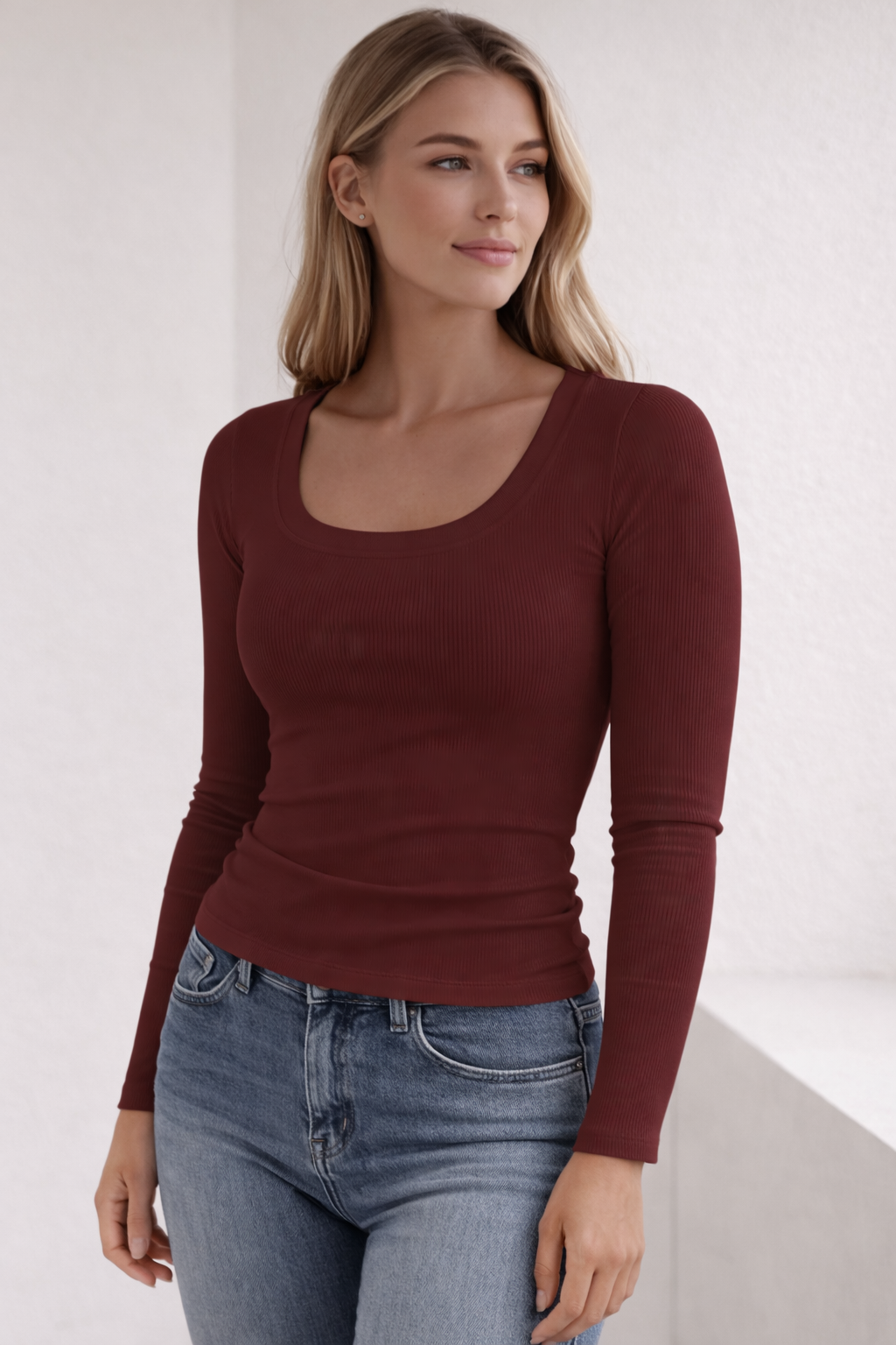 Woman wearing a burgundy long-sleeve top and blue jeans against a white background