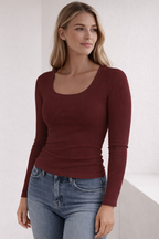 Woman wearing a burgundy long-sleeve top and blue jeans against a white background