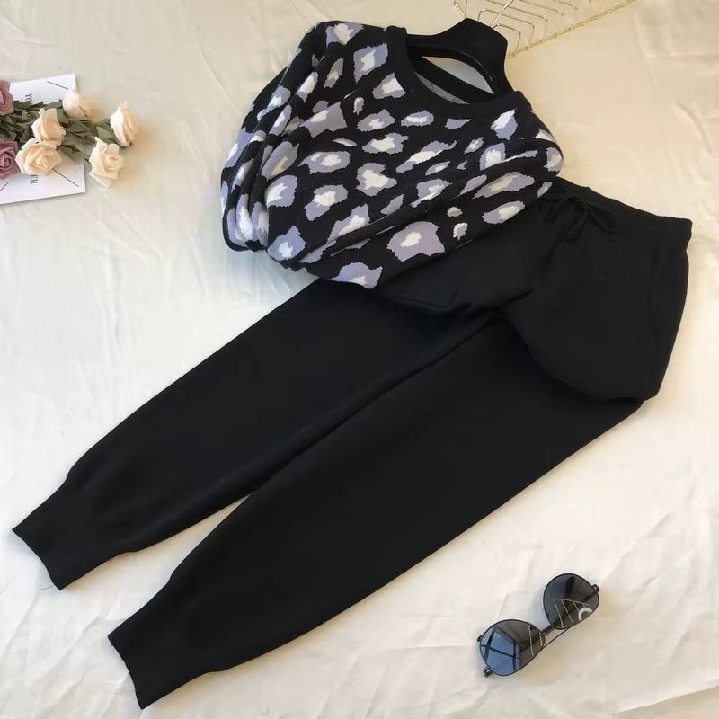 Black and white patterned top and black pants on a light surface with sunglasses and flowers.