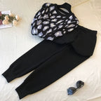 Black and white patterned top and black pants on a light surface with sunglasses and flowers.