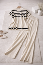 Striped top and beige pants on a light surface with shoes and a vase.