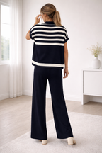 Woman wearing a black and white striped shirt and dark blue pants in a room with white walls and a window.