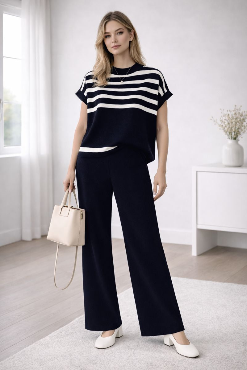 Woman wearing a black and white striped top with wide-leg pants in a minimalistic room.