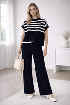 Woman wearing a black and white striped top with wide-leg pants in a minimalistic room.