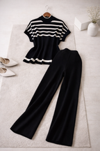 Black and white striped top and black pants on a light gray surface with shoes and a vase.