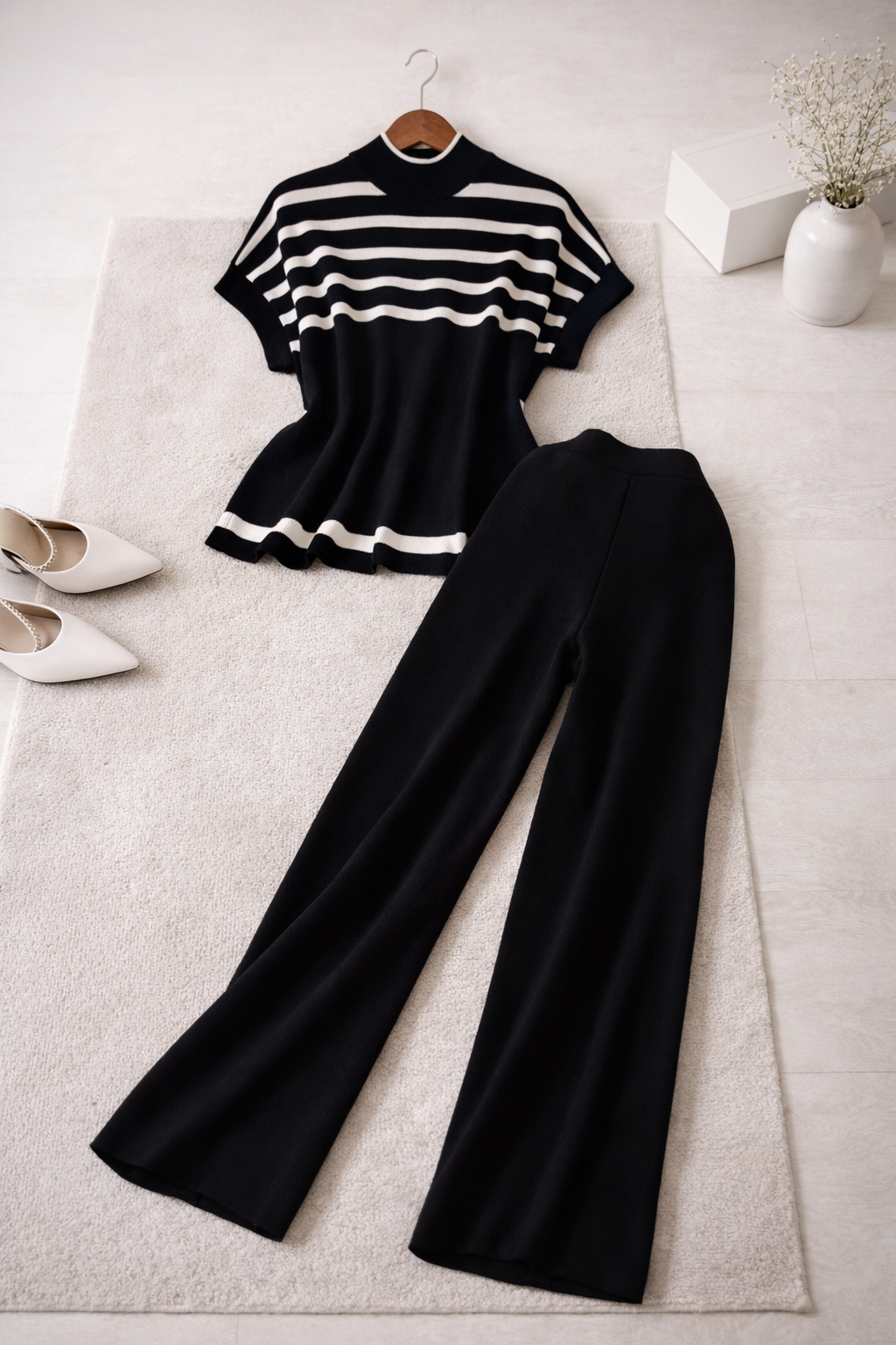 Black and white striped top and black pants on a light gray surface with shoes and a vase.