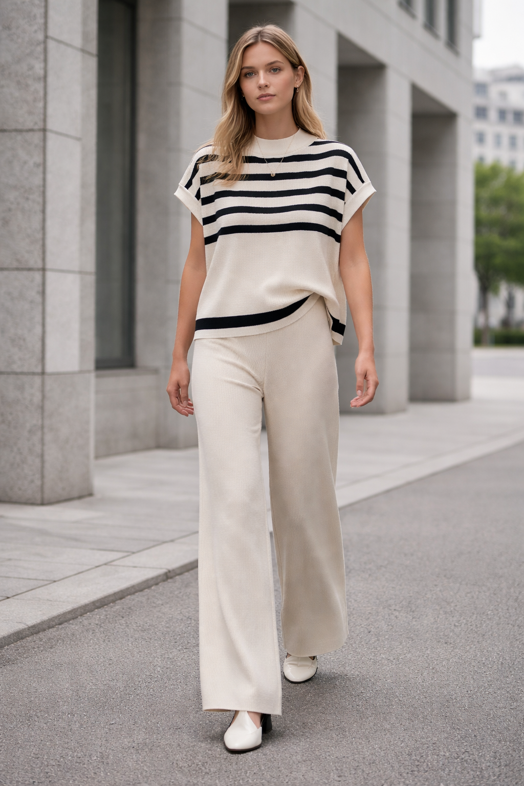 Woman wearing a black and white striped top and beige pants standing on a city street.