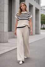Woman wearing a black and white striped top and beige pants standing on a city street.