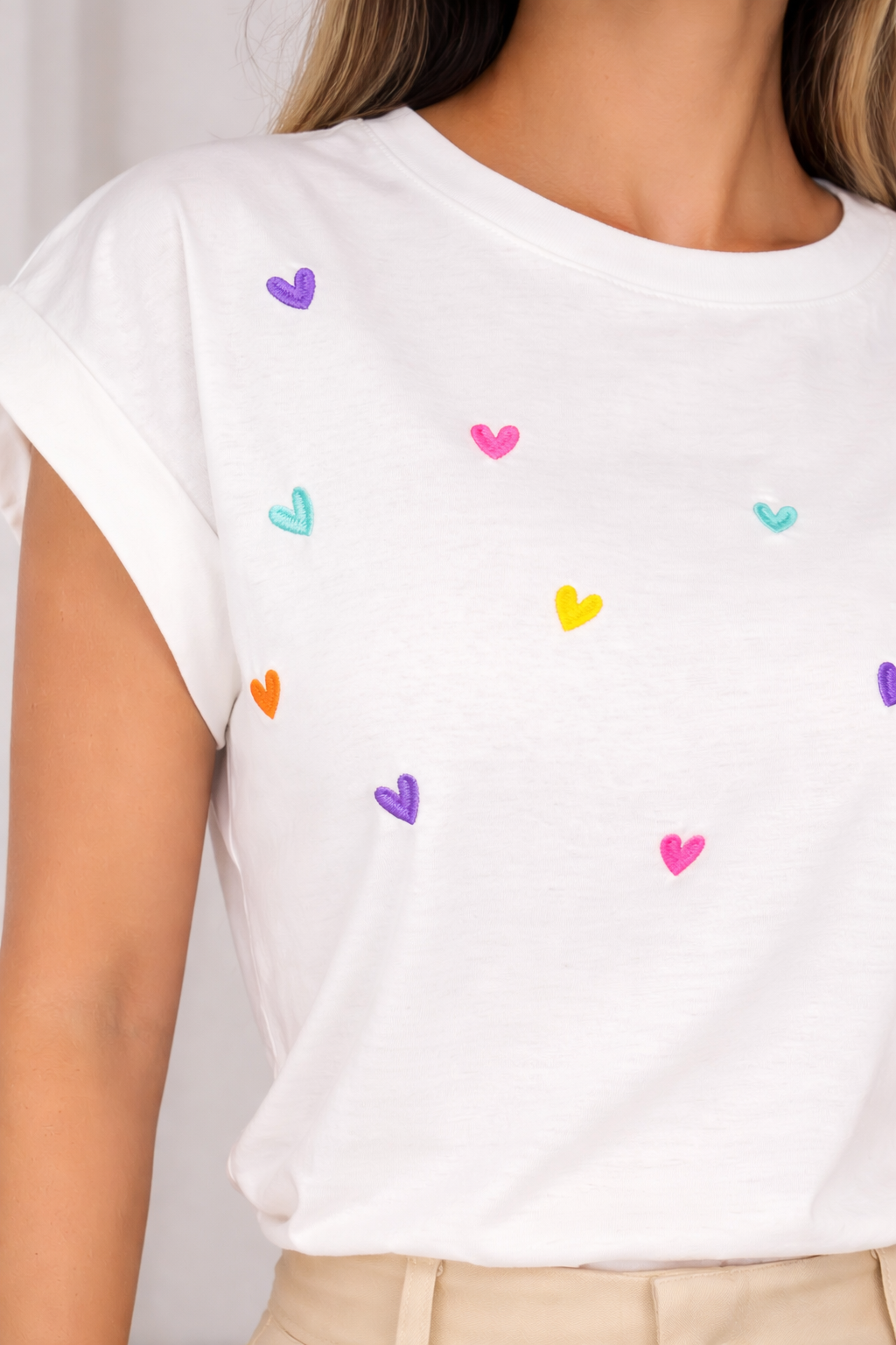 White t-shirt with colorful heart patterns worn by a person.