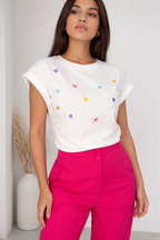 Woman wearing a white t-shirt with colorful heart patterns and pink pants against a plain background