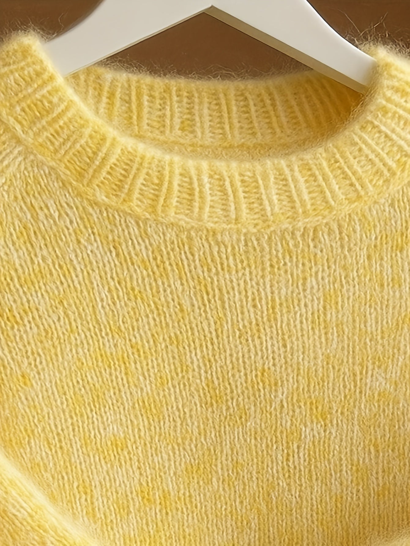 Yellow sweater on a hanger against a brown background