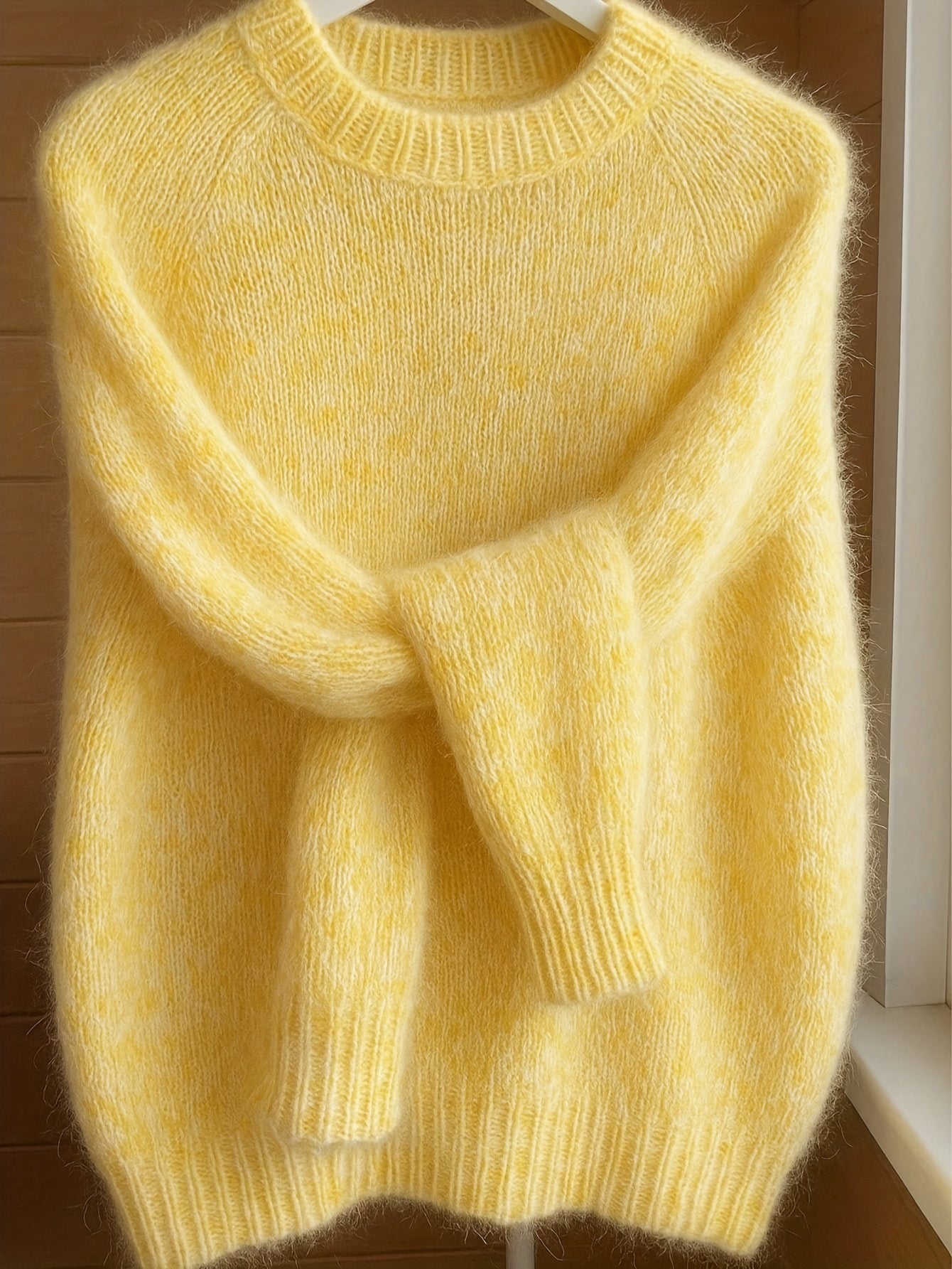Yellow sweater on a hanger against a wooden wall.