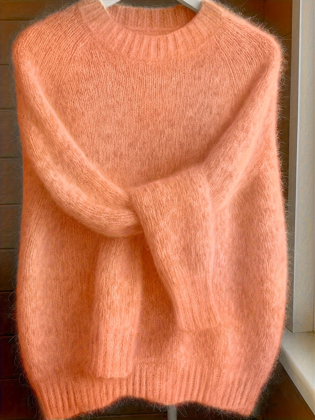 Pink sweater on a hanger against a wooden background
